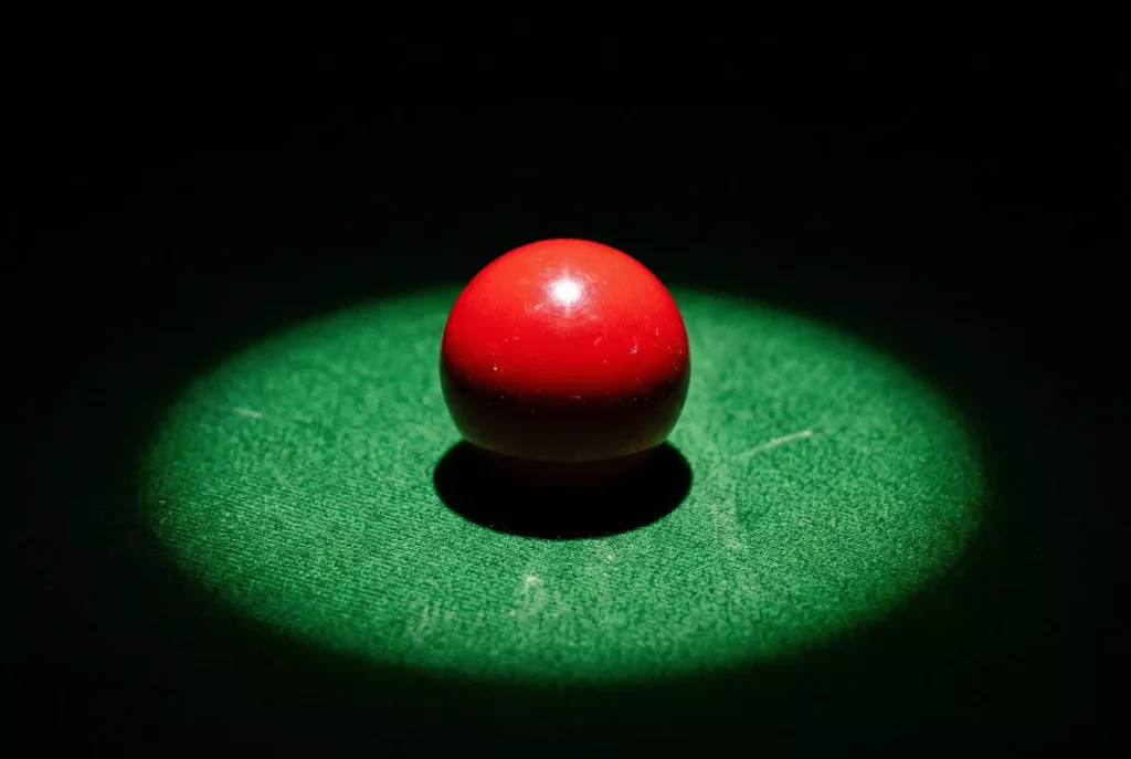 Nahaufnahme einer roten Snooker-Kugel auf dem grünen Tuch unter harter Beleuchtung als Symbol für Spielmanipulation