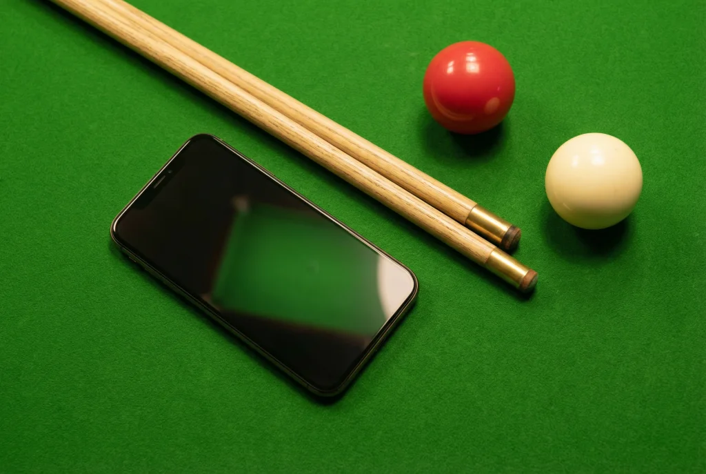 Smartphone neben einem Snooker-Queue auf grünem Tuch als Symbol für mobiles Wetten auf Snooker