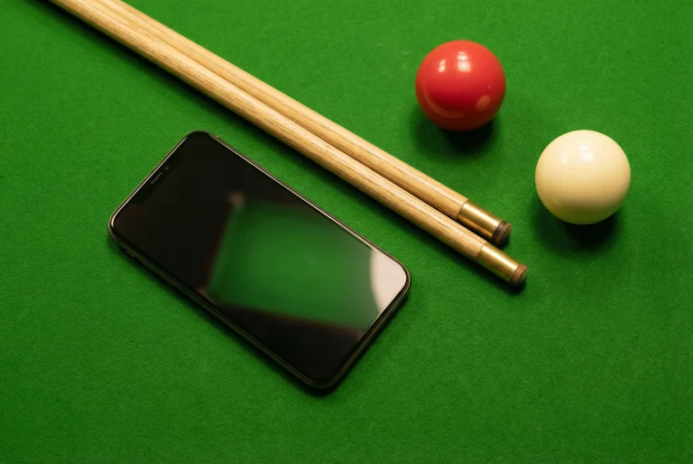 Smartphone neben einem Snooker-Queue auf grünem Tuch als Symbol für mobiles Wetten auf Snooker